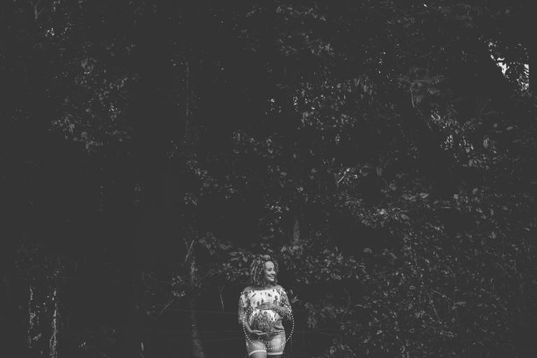 Gestante com as mãos no bebê, ao fundo árvores, foto preto e branco