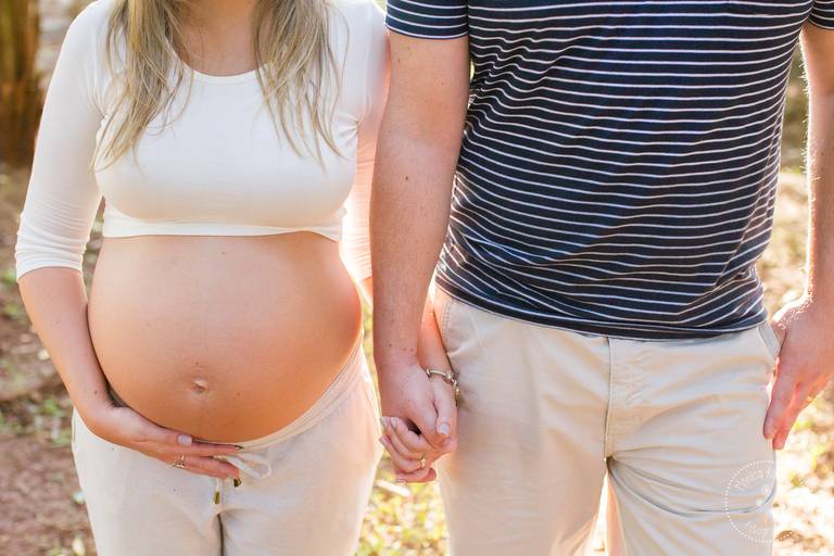 Close na barriga da gestante, que está de mãos dadas com o seu marido