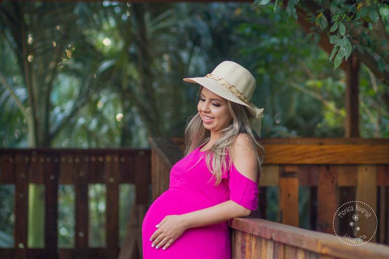 Gestante Dani com um vestido rosa e um chapéu, encostada em uma parede de madeira