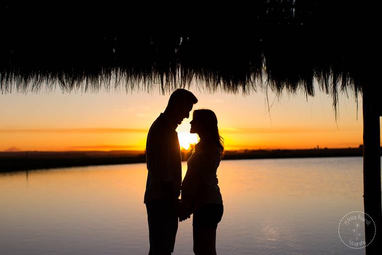Silhueta de um casal se olhando, no meio deles um por-do-sol lindo, atrás um lago lindo
