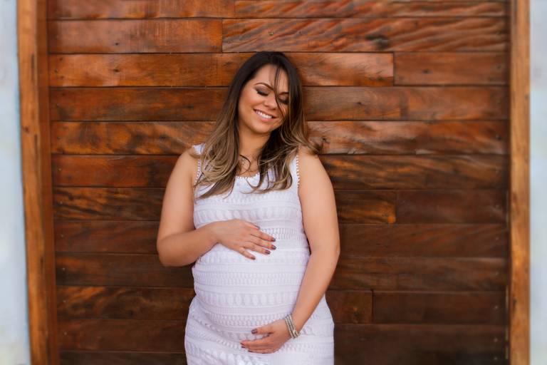 Gestante sorrindo enquanto segura seu bebê, em frente a uma porta de madeira 
