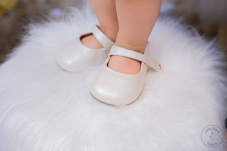 Close nos sapatinhos brancos da aniversariante, em cima de um banquinho peludinho