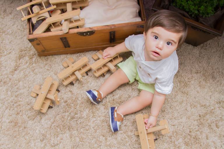Eduardo sentado no tapete com os aviõezinhos de madeira da decoração, na sua festinha de 1 ano  