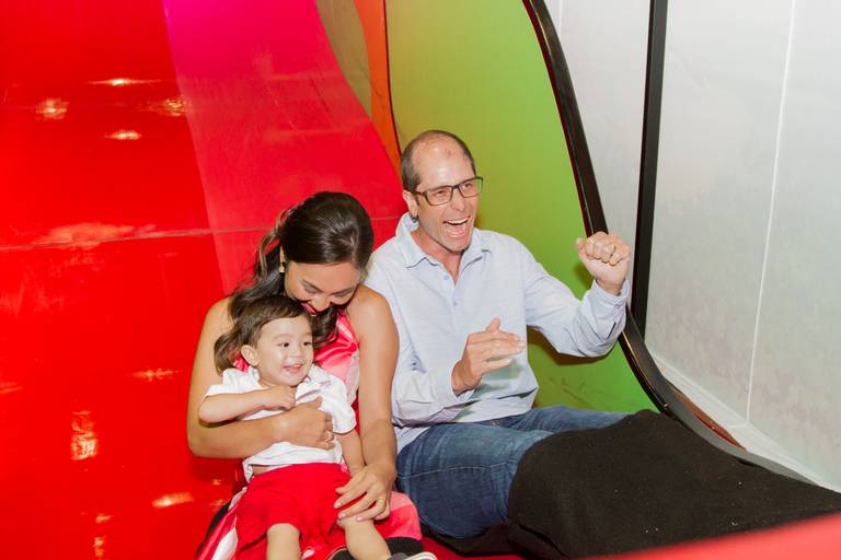 Emanuel no colo da sua mamãe e ao lado do papai, em um  escorregador vermelho