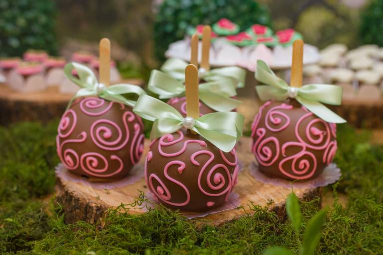 Docinho de maça coberto por chocolate e decorado com desenhos rosas, em um palito 