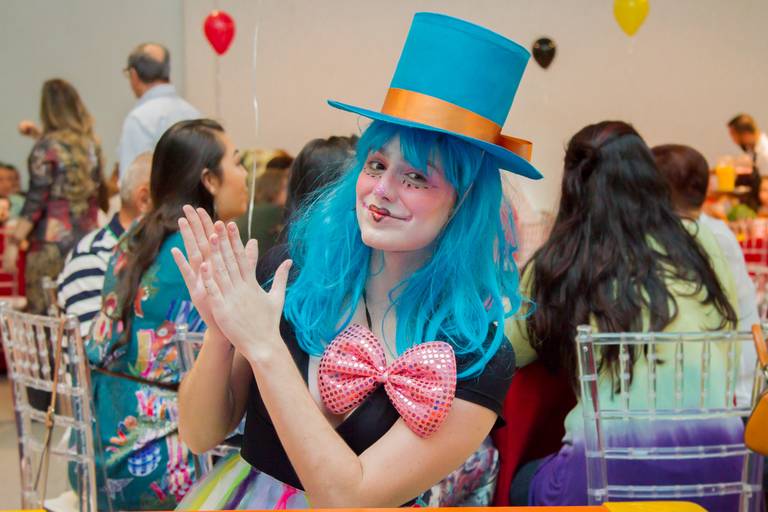 Palhacinha de cabelo azul e chapéu azul, com as bochechas pintadas de rosa e com um coração desenhado na boca 