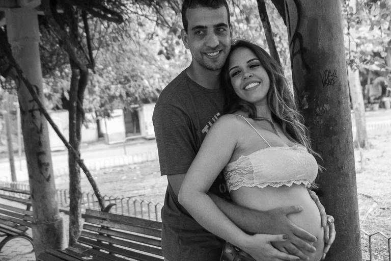 Gestante e o marido sorrindo para a câmera em um parque no Rio de Janeiro