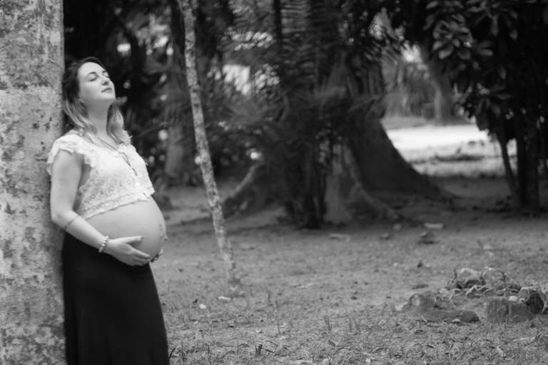 Gestante segurando a barriga apoiada em um tronco de árvore no Jardim Botânico no Rio de Janeiro