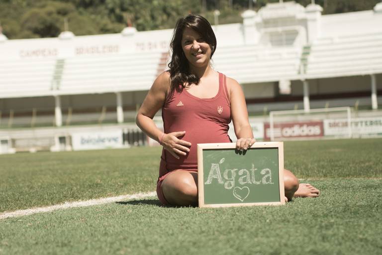 Gestante segurando a barriga com uma lousa na frente com o nome da filha no gramado do Fluminense Football Club no Rio de Janeiro