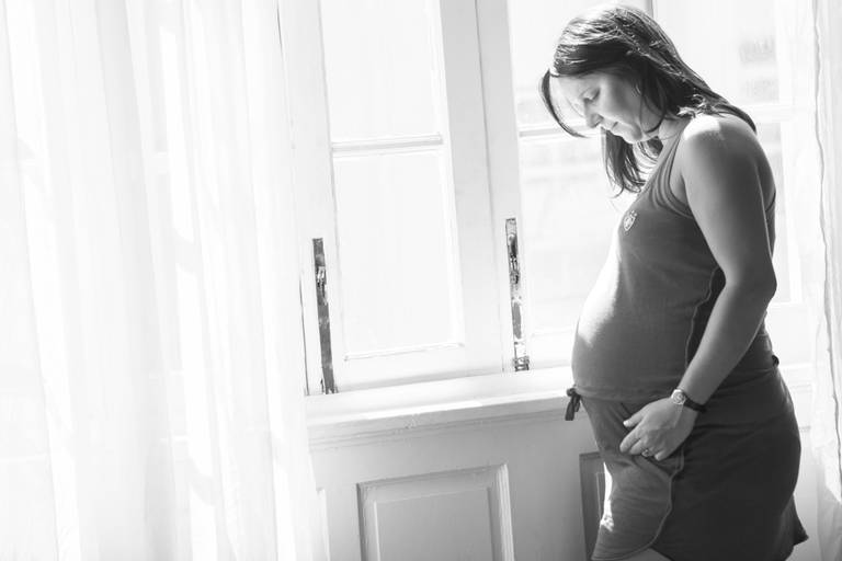 Gestante olhando para sua barriga em frente a uma janela no Fluminense Football Club no Rio de Janeiro