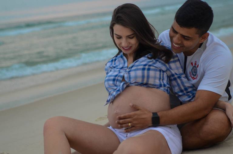 Casal Grávido surpreso, olhando para a barriga da gestante no momento em que o bebê se mexeu em frente ao mar  no Quebra Mar na Praia da Barra da Tijuca no Rio de Janeiro