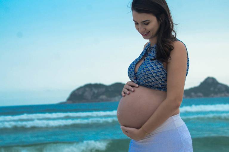 Grávida feliz olhando para a sua barriga em frente ao ar no Quebra Mar na Praia da Barra da Tijuca no Rio de Janeiro