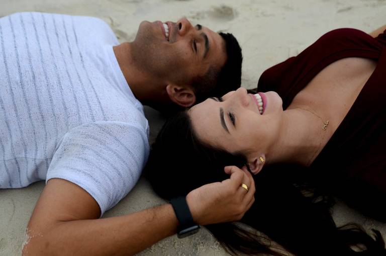 Casal Grávido sorrindodo deitados na areia no Quebra Mar na Praia da Barra da Tijuca no Rio de Janeiro