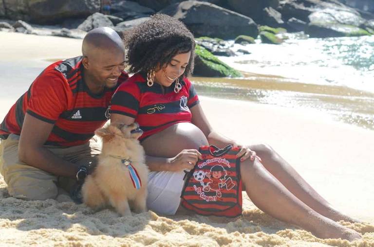 Casal Grávido olhando para a barriga da gestante Casal Grávido sorrindo com um cachorrinho em frente ao mar  na Praia Vermelha no Rio de Janeiro