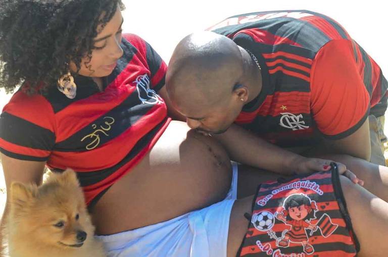 Casal Grávido na Praia com o marido beijando a barriga da gestante com um cachorrinho em frente ao mar  na Praia Vermelha no Rio de Janeiro