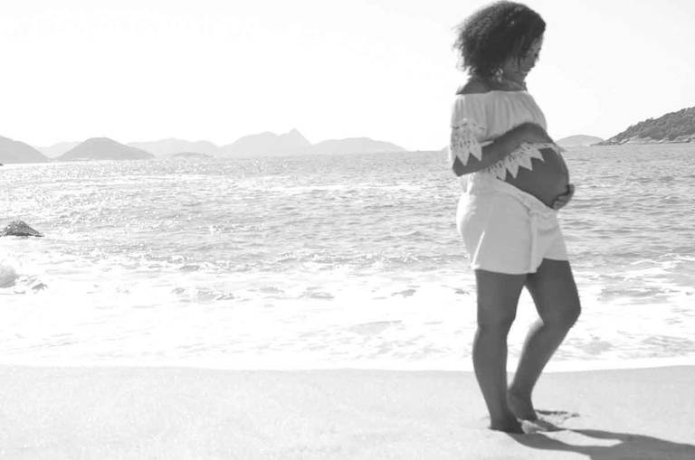 Gestante sorrindo olhando para a barriga em frente ao mar  na Praia Vermelha no Rio de Janeiro