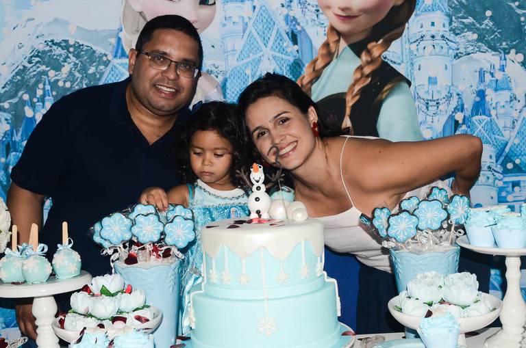 Menina posa com os pais em frente ao seu bolo e decoração de Frozen em sua festa infantil de aniversário em Botafogo no Rio de Janeiro