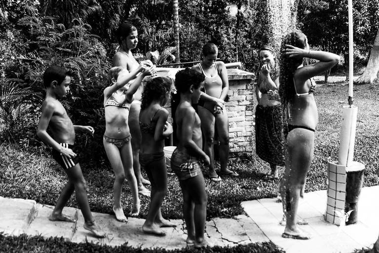 Crianças esperando em uma fila para tomar banho de chuveiro em uma festa infantil ao ar livre 