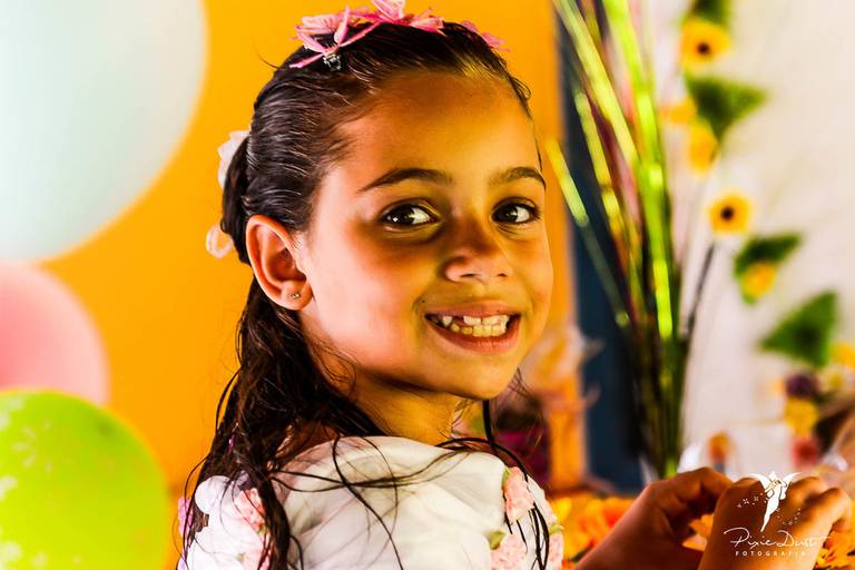 Menina sorrindo para a câmera em frente a decoração da sua festa infantil de aniversário
