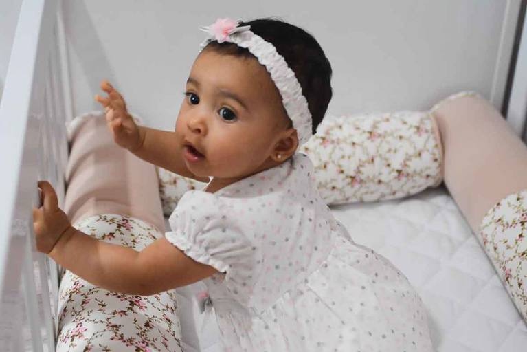 Bebê de vestido branco no bercinho 