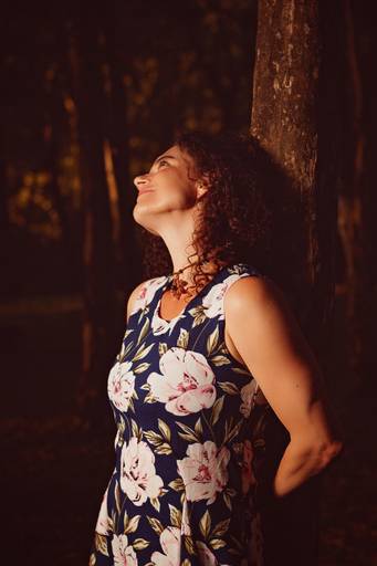 Modelo bem iluminada com flash em uma área de mata fechada encostada em uma árvore olhando para cima