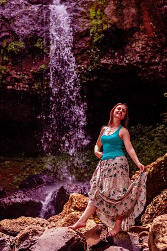 Modelo balançando a saia e segurando na cintura em frente a cachoeira 