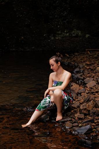 Modelo vestindo tomara que caia com estampa florida sentada na beira do rio e com um pé na água