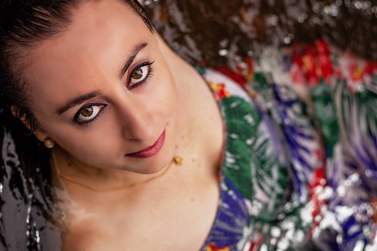 Modelo vestindo tomara que caia com estampa florida deitada na água com cabeça inclinada olhando para a câmera