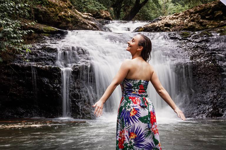 Modelo vestindo tomara que caia florido de pé em frente à cachoeira de costas para a câmera e com queda em véu de noiva