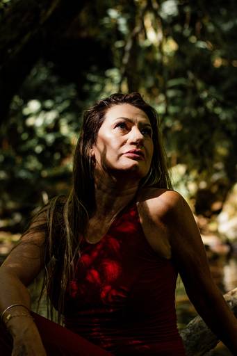 Mulher usando macacão vermelho sobre os grafismos produzidos pela sombra das árvores