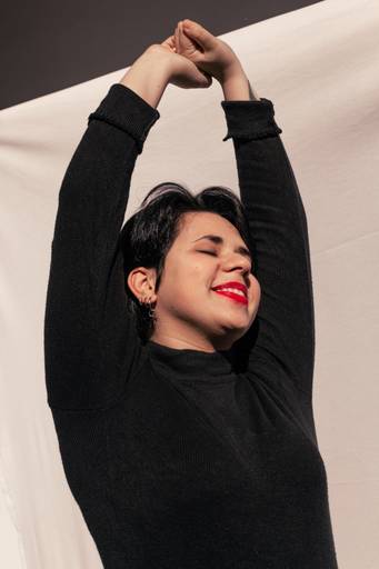 Bianca com os braços estendidos, com fundo branco em ensaio individual no quintal de sua casa, na região de São Paulo Capital.