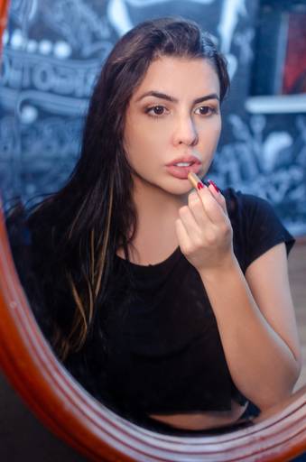 Ensaio fotográfico sensual da Bia numa barbearia, passando batom em frnte ao espelho.