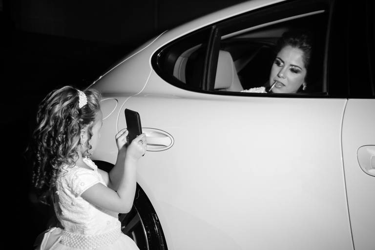 Noiva vilma passando o batom enquanto noivinha segura o espelho na entrada da igreja antes do casamento