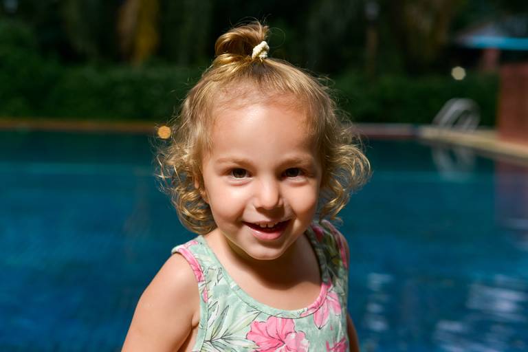 Pequeña niña rubia sonriendo. Retrato infantil en exterior día de lluvia con una piscina de fondo. Marcos Pasquare fotografía de