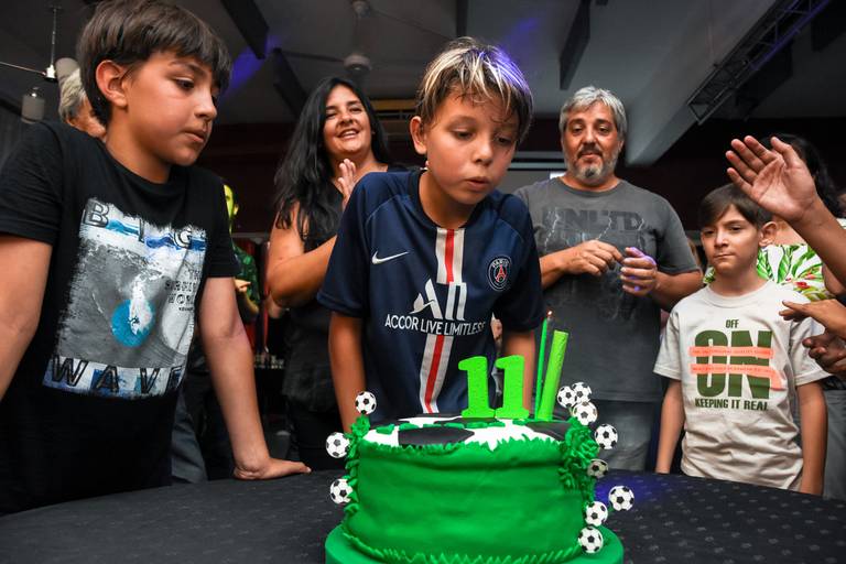 Nño sopla las velas en su cumple futbolero. Retrato infantil en exterior día de lluvia con una piscina de fondo. Marcos Pasquare fotografía de