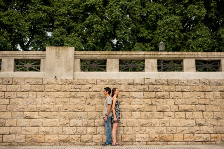 Sesión pre boda en la Costanera Sur, CABA. Novios espalda con espalda, sobre la pared y por encima las hojas verdes de los árboles. Reserva ecológica. Marcos Pasquare Fotógrafo de Bodas.