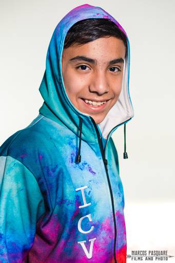 alumno posa con la campera de egresados y tiene la capucha puesta. Campera de egresados azul estampada. Sonrisa. Morocho. Marcos Pasquare Fotografía escolar.