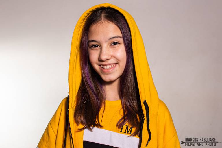 Alumna con campera de egresados, pelo teñido de violeta y una sonrisa grande. Marcos Pasquare Fotografía escolar.