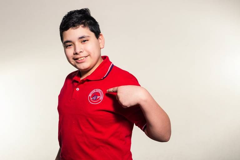 Alumno de quinto grado del instituto canto a la vida de Villa Lugano se señala con el índice el logo de su colegio. Un retrato original.  Marcos Pasquare Fotografía escolar. 