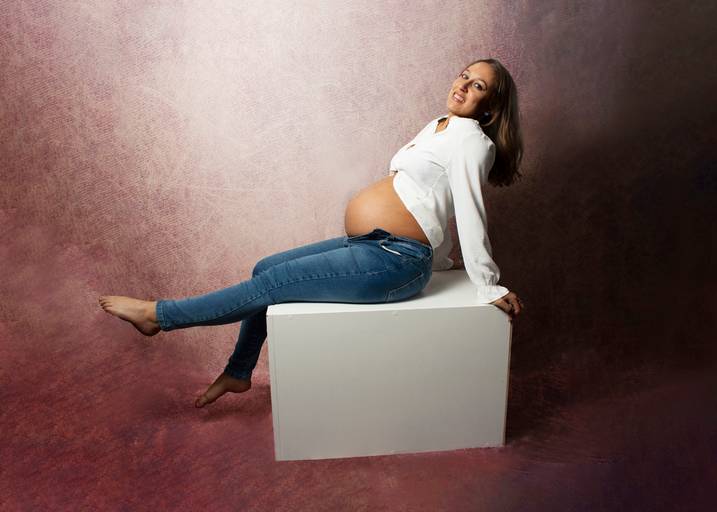 embarazada sentada sobre cubo blanco con ropa casual, en  interior