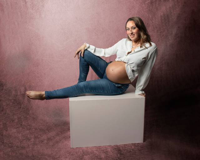 embarazada sentada sobre cubo blanco con ropa casual, en interior