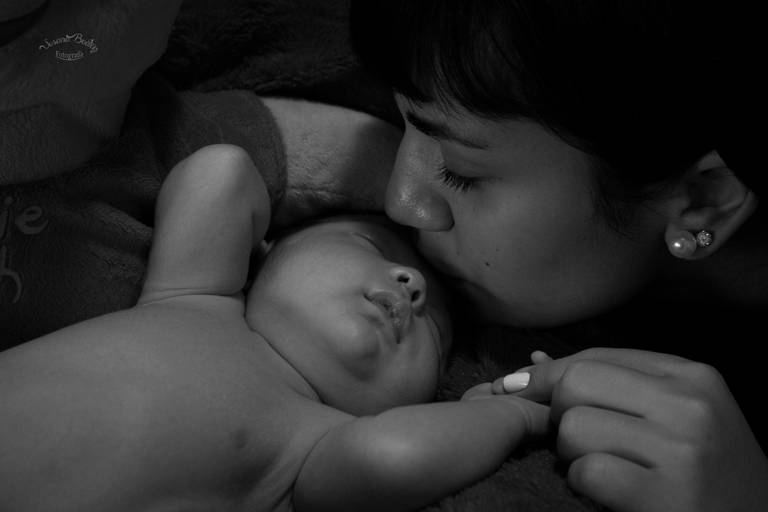 Newborn - Bebe boca arriba, besado por niña, en blanco y negro