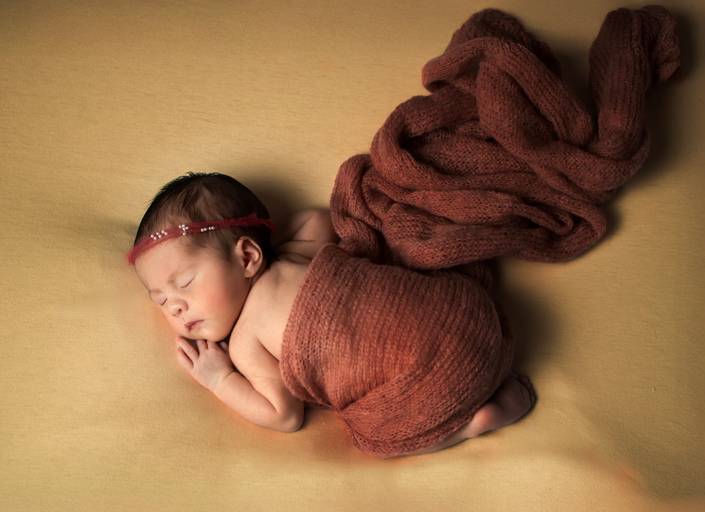 newborn - Fotografía newborn de recién nacido en pose colita arriba, envuelto en manta naranja terroso sobre fondo cálido. 