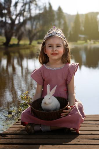 Niña sentada en un muelle con una sesta con un conejo con un lago detrás, fine art