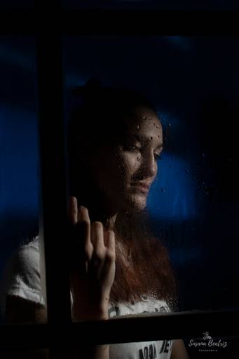 retrato chica mirando a través de una ventana un dia de lluvia