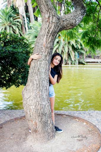 quinceañera asomada detras de un arbol