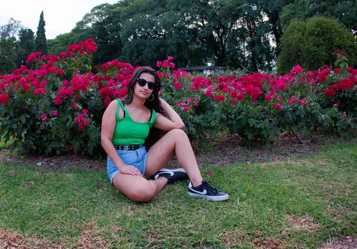 quinceañera con lentes sentada delante de rosas rojas