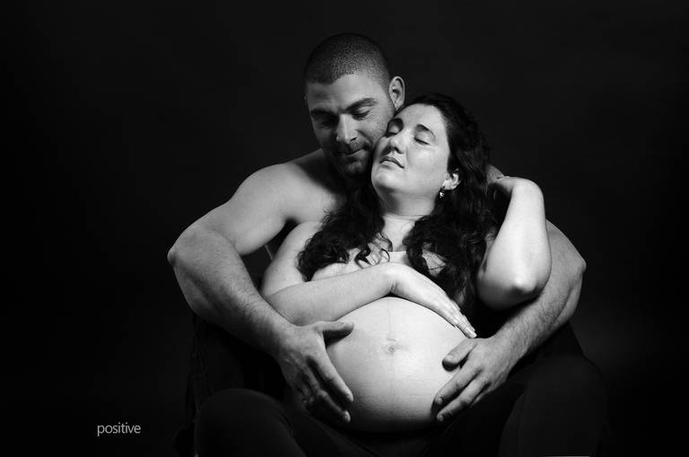 Mujer embarazada con su pareja abrazándola por detrás, en blanco y negro, con fondo oscuro - Cristian Moriñigo, fotógrafo de Roldán