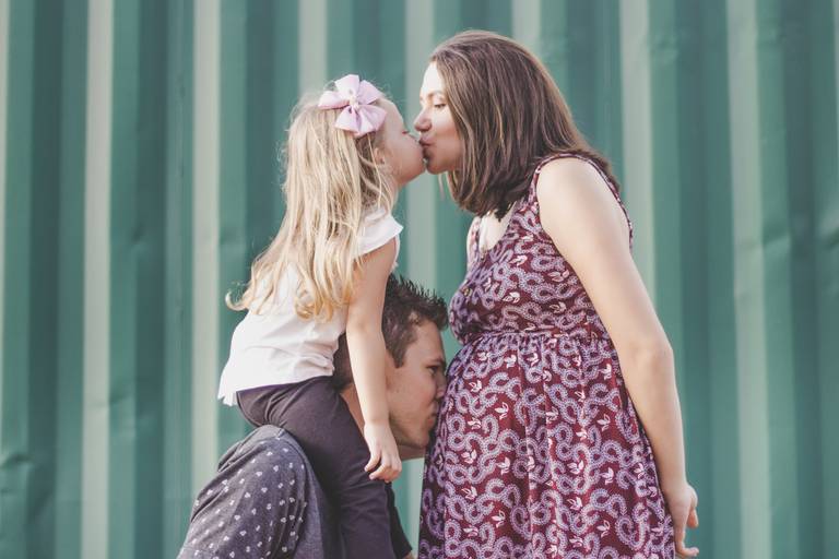 foto de pai beijando a barriga e mãe beijando filha mais velha em ensaio gestante