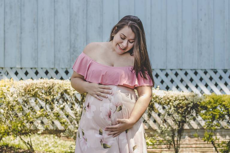 mamãe em cenário de cerca viva e parede de madeiras admirando barrigão